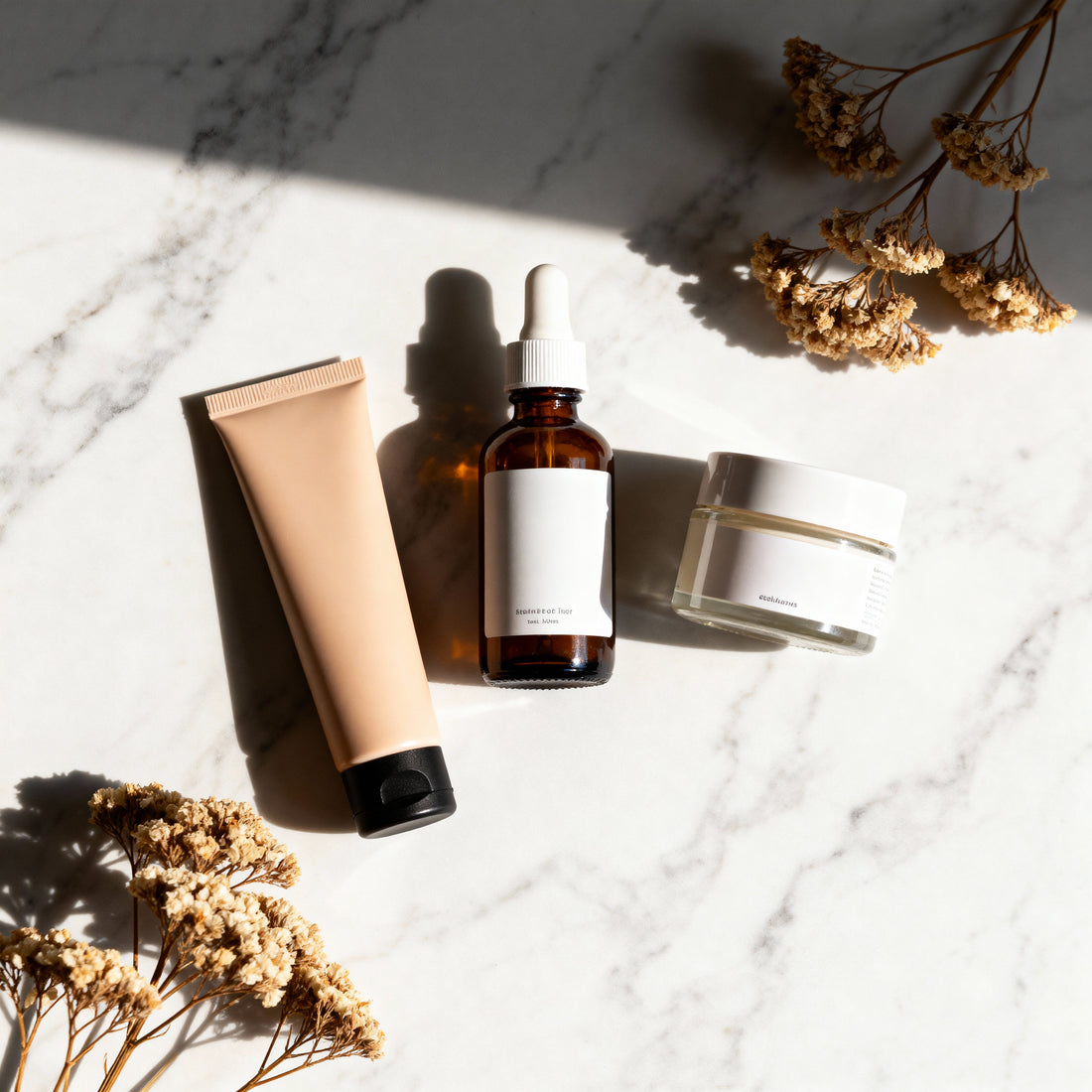 Natural lash and brow care products with botanical dropper bottle and dried flowers on marble background